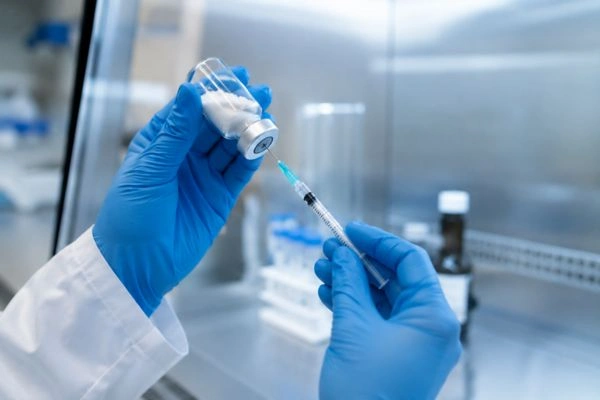 Gloved hands reconstituting peptide vial in laboratory